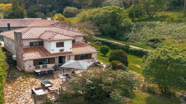 Ein zweigeschossiges Steinhaus mit Ziegeldach, einer Terrasse mit Gartenmöbeln und einem gepflegten Garten.