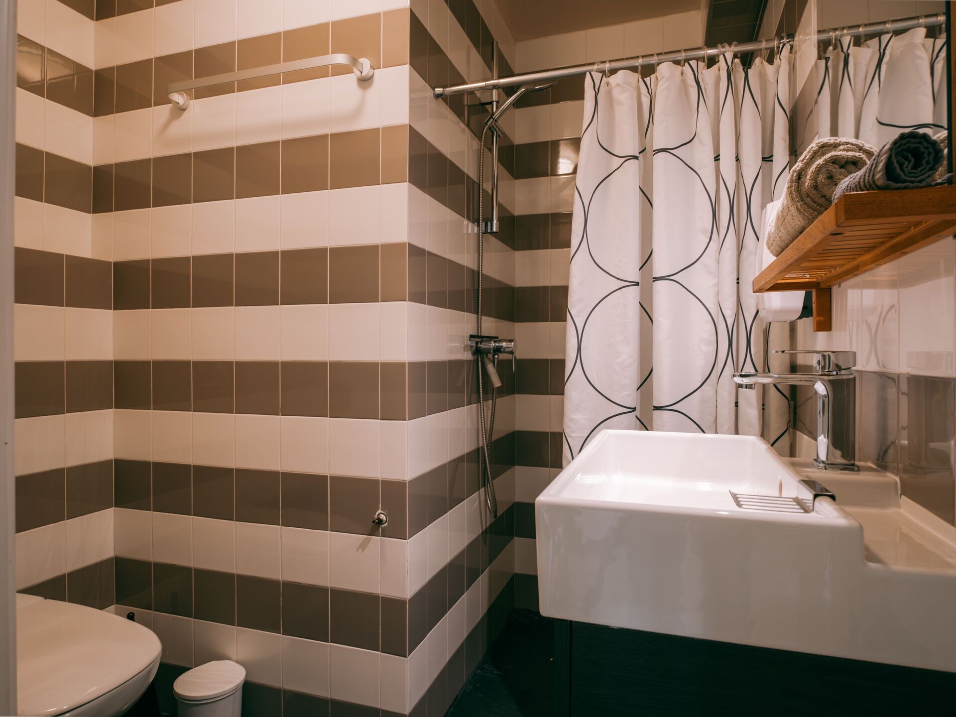 Une salle de bain avec des murs recouverts de carreaux à rayures, un lavabo blanc et un rideau de douche orné d’un motif circulaire.
