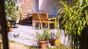 Un patio con dos sillas de madera y una mesa, rodeado de plantas en macetas y una valla decorativa.