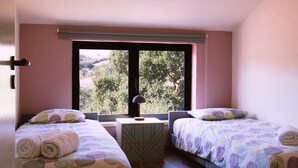 Un dormitorio con dos camas, una mesita y una ventana con vistas a la vegetación.