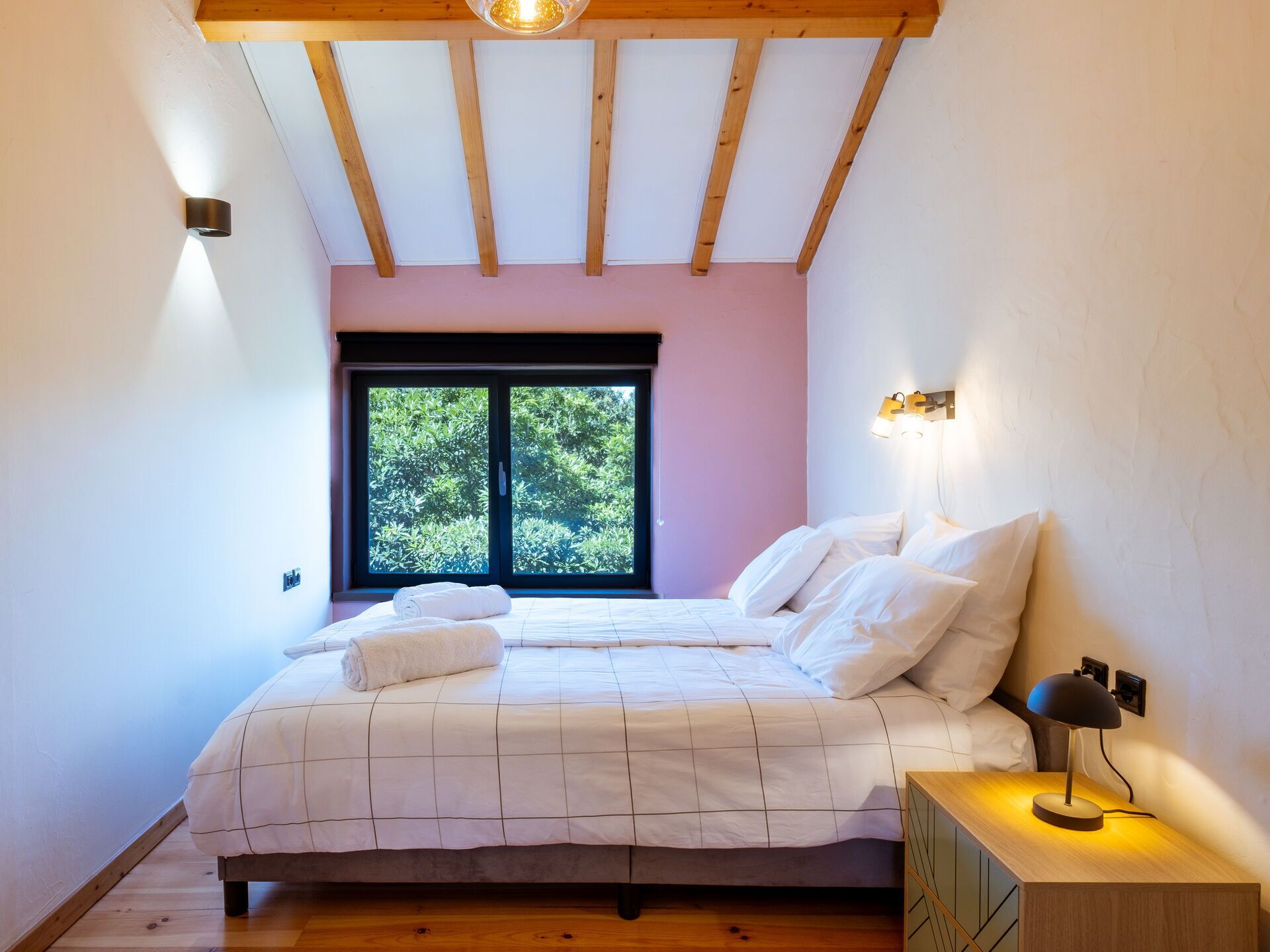 A bedroom with a bed, a nightstand, a lamp, a window, and a ceiling light.