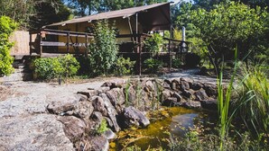A rustic wooden structure with a covered porch, surrounded by greenery and a small pond. - Casa Cha – Luxury Safari Tent with Oriental Flair at Quinta Japonesa (Carvalhal Benfeito)