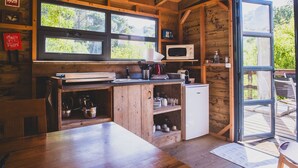 A compact kitchen with wooden cabinetry, a microwave, and a refrigerator. Large windows provide natural light and a view of the outdoors. - Casa Cha – Luxury Safari Tent with Oriental Flair at Quinta Japonesa (Carvalhal Benfeito)
