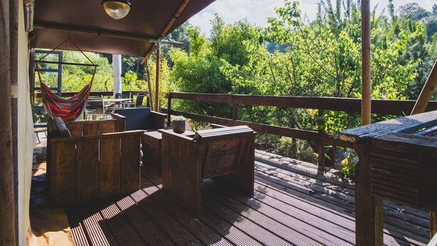 A wooden deck with a hammock, seating area, and a view of lush greenery. - Casa Cha – Luxury Safari Tent with Oriental Flair at Quinta Japonesa (Carvalhal Benfeito)