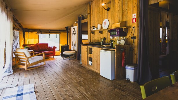 Un interior acogedor de cabaña con suelo de madera, un sofá rojo, una pequeña cocina con microondas y una mesa de comedor.