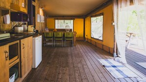 Cocina pequeña con armarios de madera, un refrigerador, un microondas y un lavamanos. Hay tres sillas verdes alrededor de una mesita con un florero.