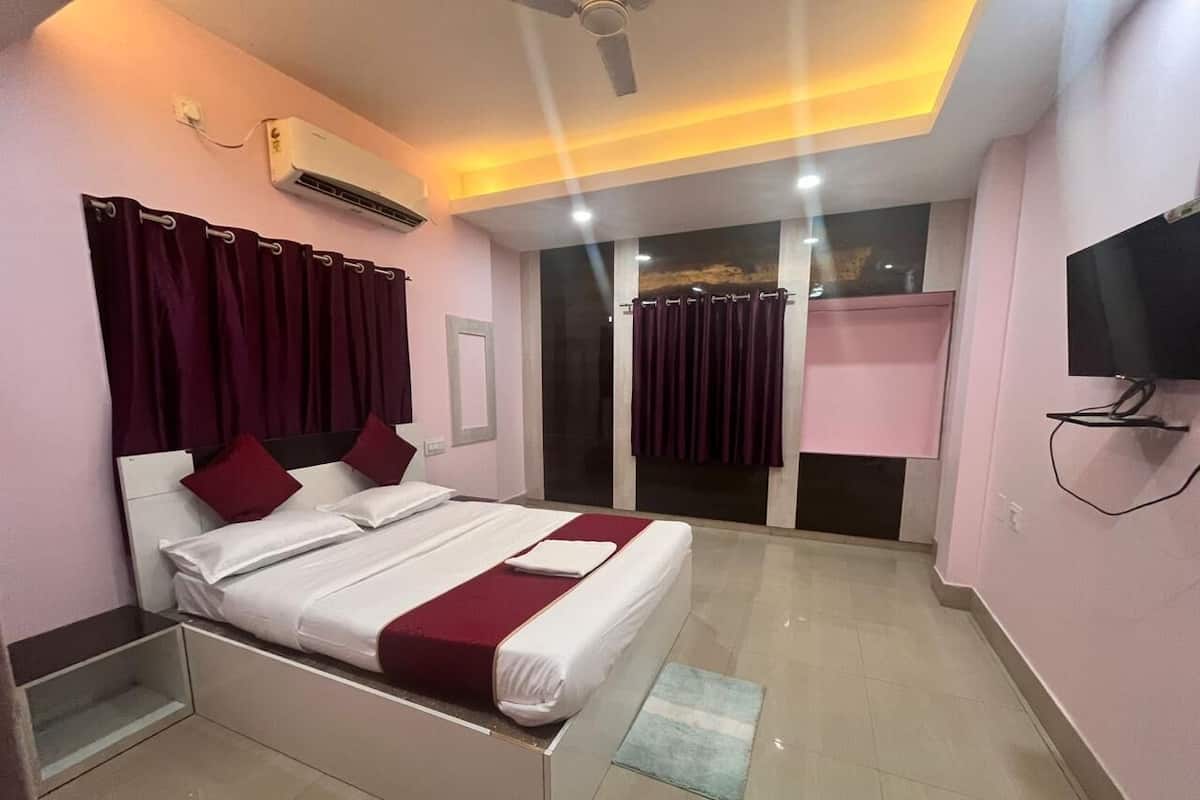 A bedroom with a bed, curtains, a TV, and an air conditioning unit.