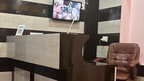 A reception desk with a flat-screen TV mounted above it, a brown leather chair, and a QR code sign. - Hotel Miracle Stay (Bhubaneshwar)
