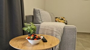 Un salon moderne avec un canapé gris, une table basse ronde en bois, un saladier rempli de fruits, une plante en pot et une télécommande.