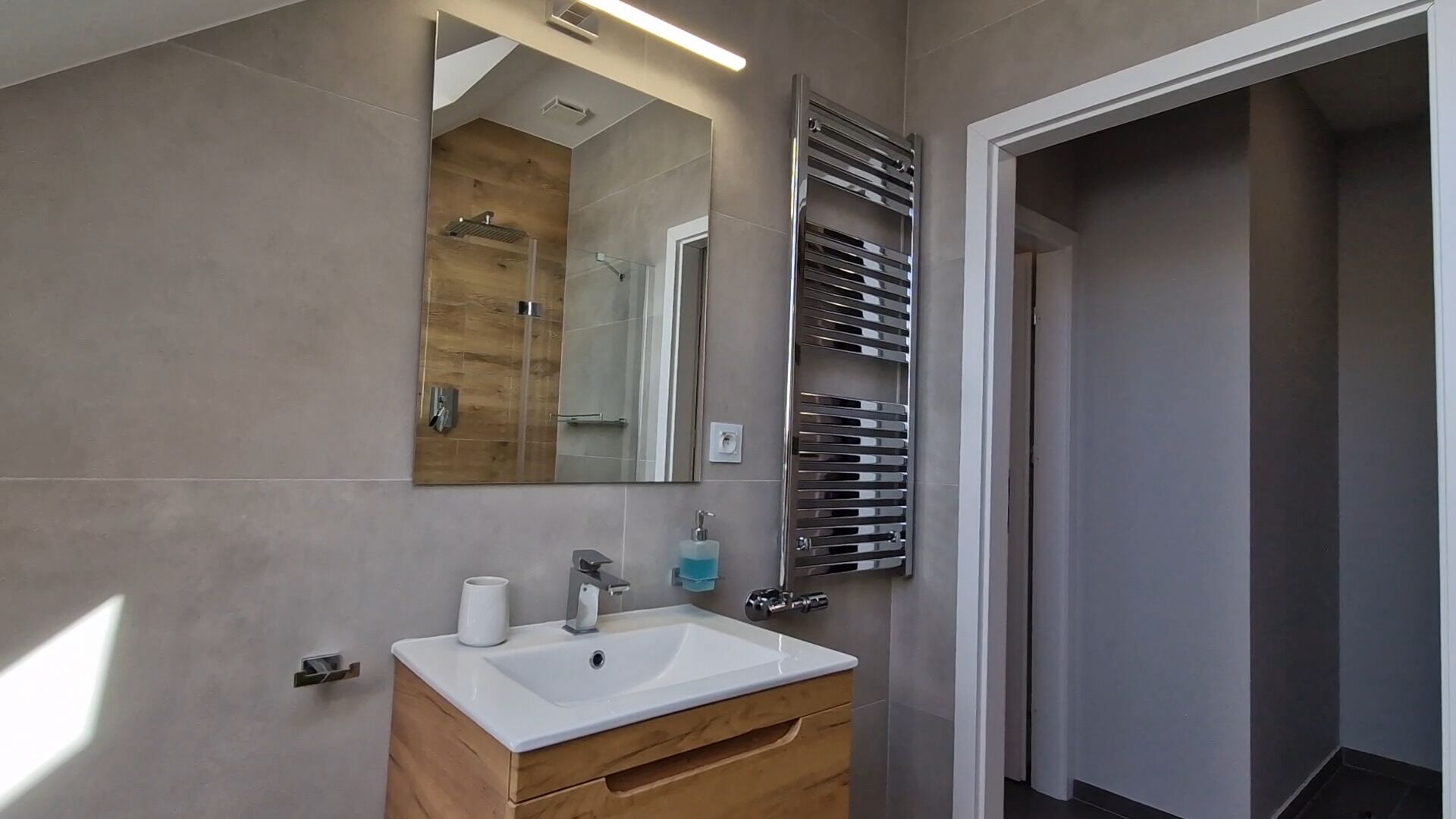 A modern bathroom with a wooden vanity, a large mirror, and a chrome towel rack.
