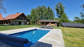 Une piscine avec une terrasse, un espace extérieur couvert aménagé en salon et des panneaux solaires.