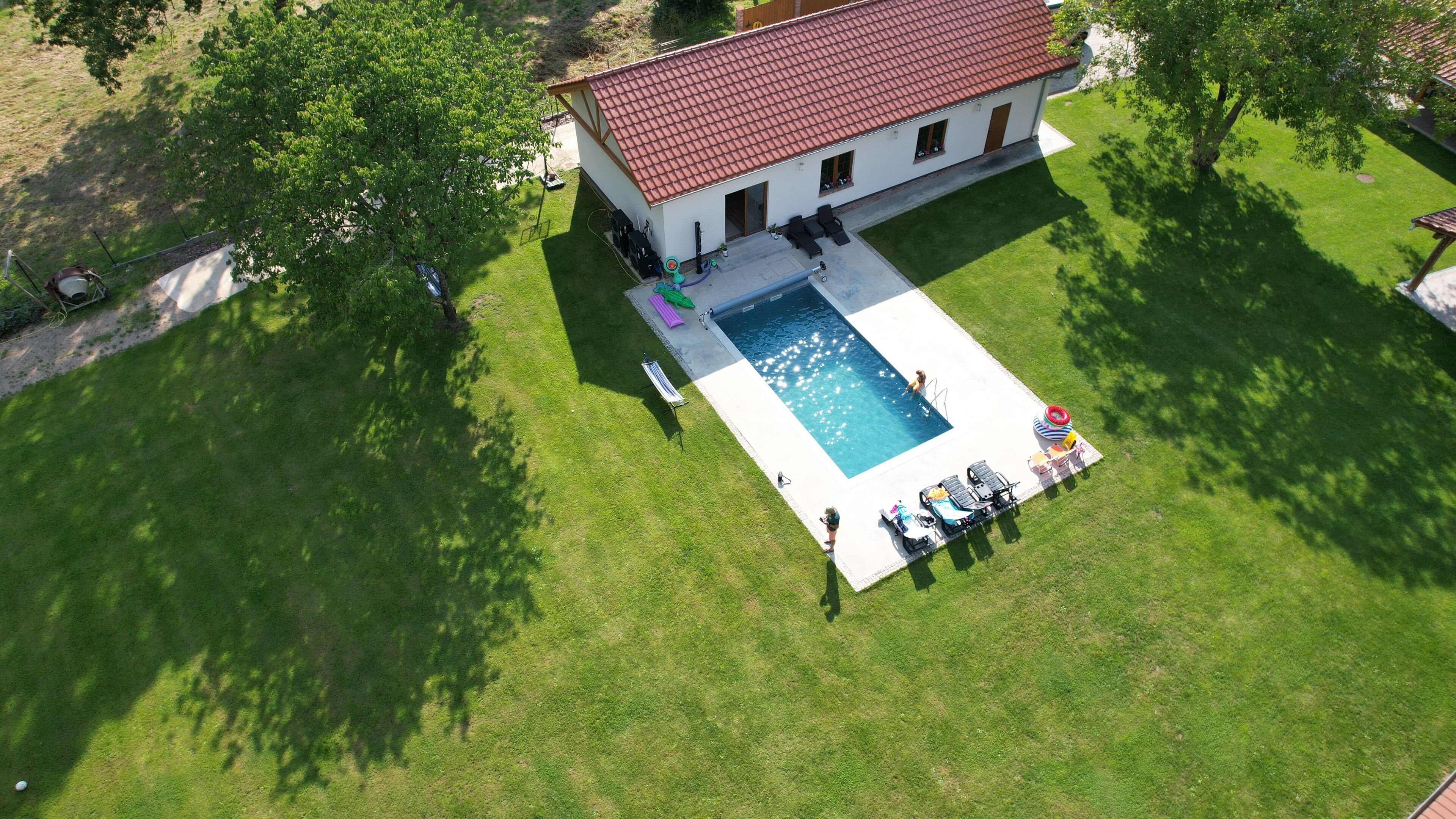 An aerial view of a house with a swimming pool, surrounded by a well-maintained lawn and trees.