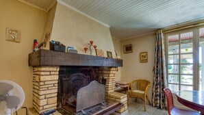 A room with a stone fireplace, a dining table, wicker chairs, and a fan.