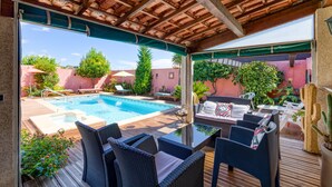 An outdoor pool area with lounge chairs and a table, surrounded by greenery and a wooden deck.