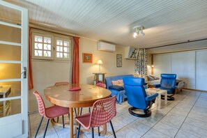 Et værelse med et spisebord, stole, en sofa, en blå lænestol, en lampe og et vindue med gardiner.