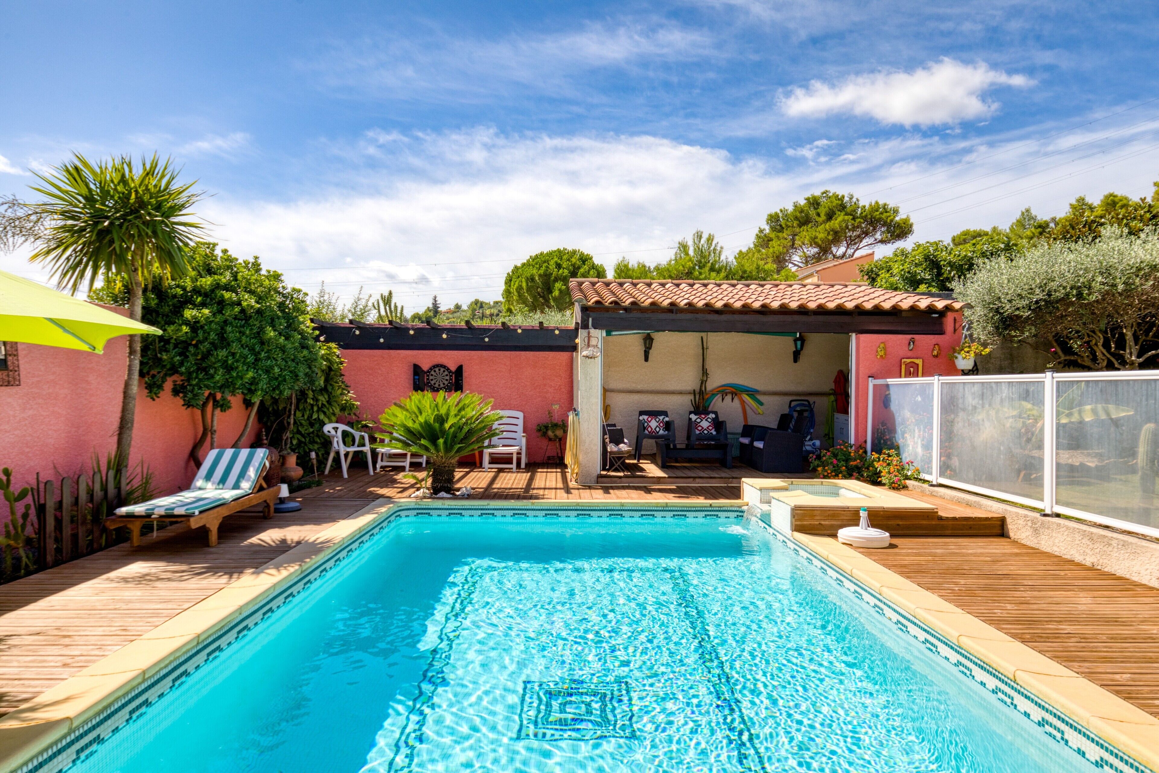 A swimming pool with a wooden deck, lounge chairs, and a covered seating area.