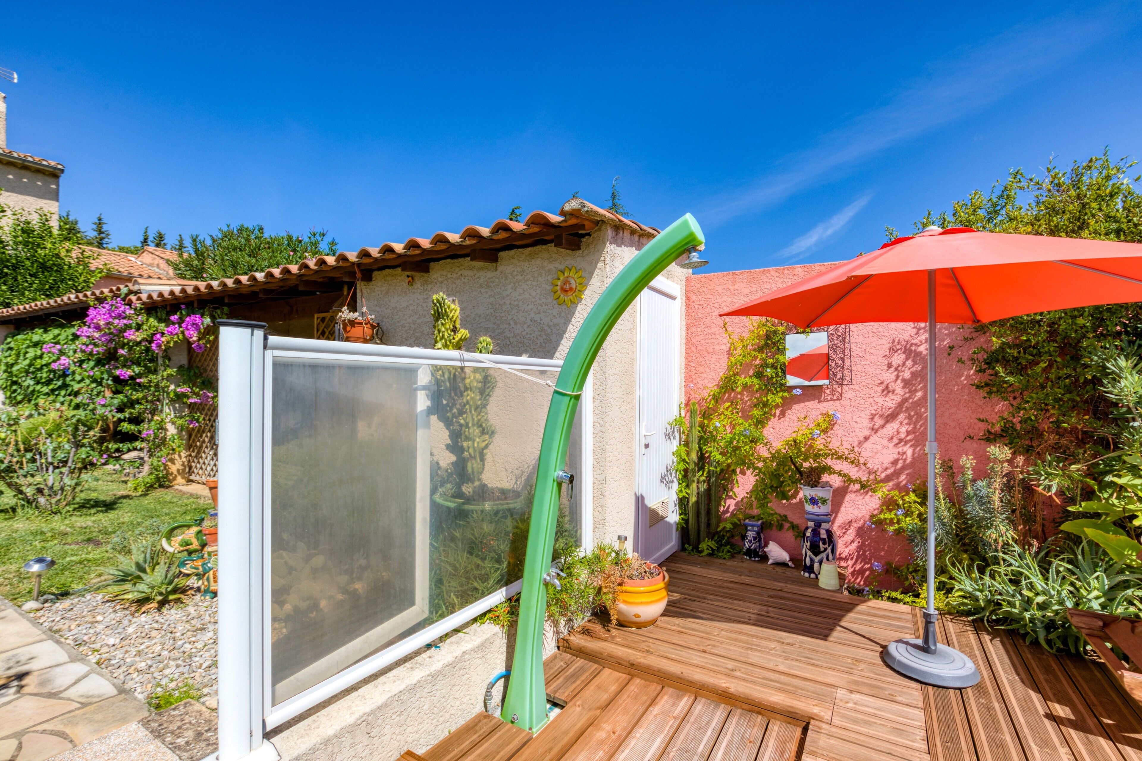 Eine Holzterrasse mit Glastür, einem roten Sonnenschirm und einem Blumentopf.
