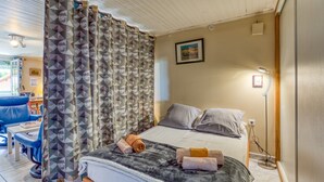 A bedroom with a bed, pillows, a blanket, a towel, a curtain, a bedside lamp, and a picture on the wall.