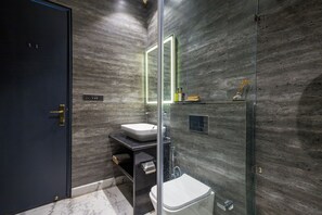 Une salle de bain moderne avec une douche à l’italienne en verre, un lavabo blanc et une porte sombre.