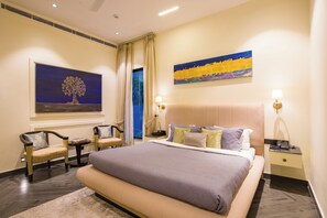 Une chambre d’hôtel avec un grand lit, deux fauteuils, une table de chevet avec une lampe et des œuvres d’art accrochées aux murs.