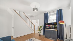 A modern living room with a staircase, a flat-screen TV, a red floor lamp, and a blue sofa. - The Modern Cwtch House - Swansea (Gorseinon)