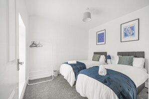 Habitación de hotel moderna con dos camas, alfombra gris, paredes blancas y una lámpara en el techo.