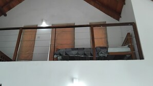 A room with a sloped ceiling, a bed with a striped blanket, a wooden chair, and a window with curtains. - The Essence (Nuwara Eliya)