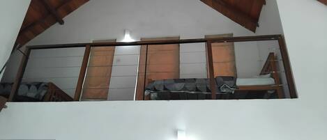 A room with a sloped ceiling, a bed with a striped blanket, a wooden chair, and a window with curtains.