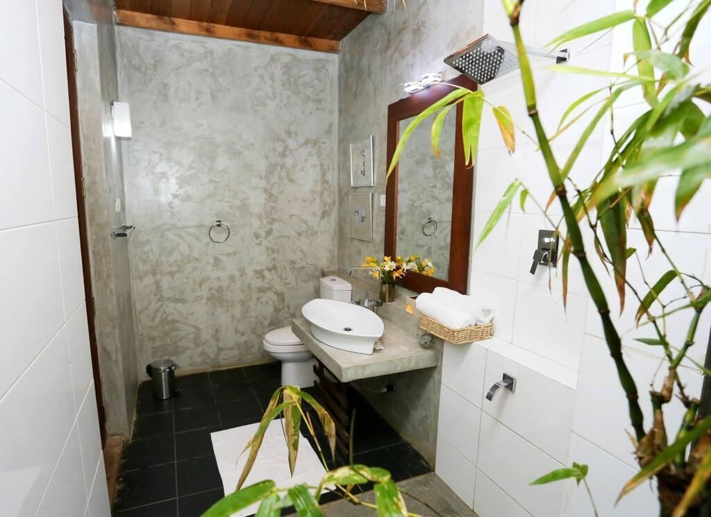 A bathroom with a marble wall, a wooden ceiling, a white sink, a toilet, a shower, and a mirror.