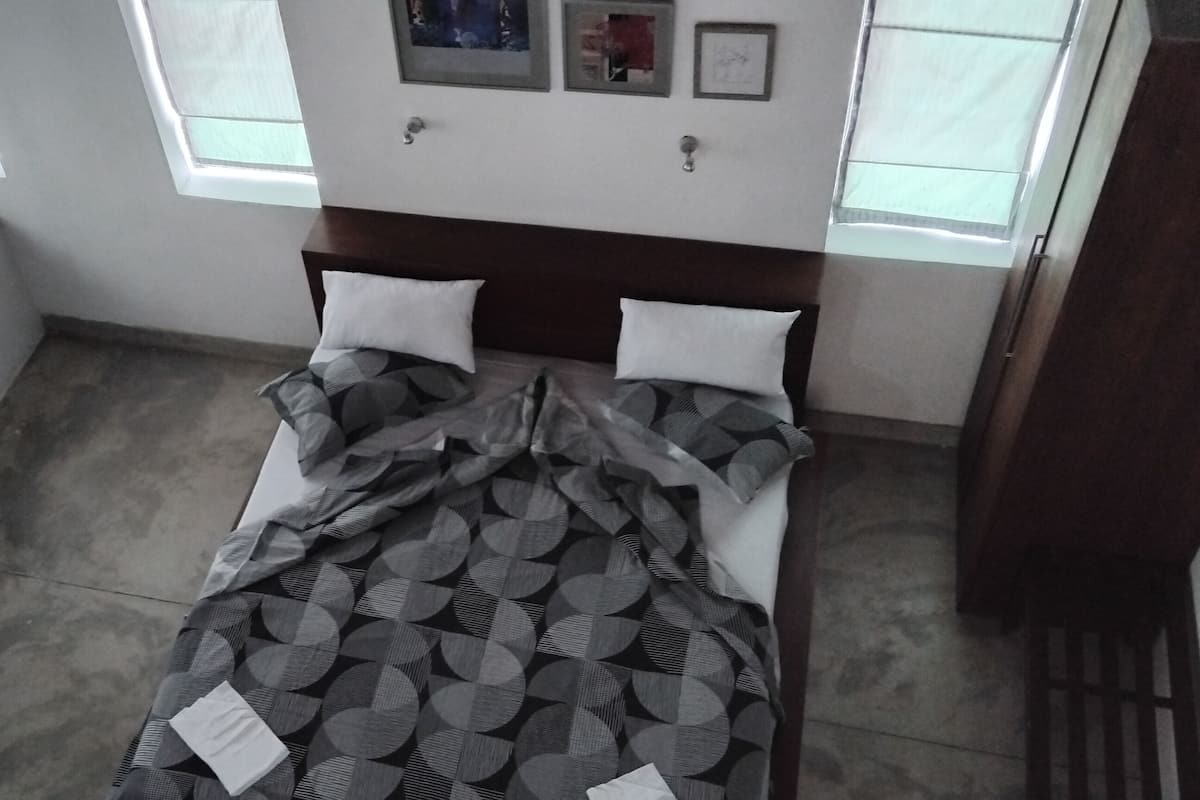 Un dormitorio con cama, un asiento junto a la ventana y un televisor montado en la pared.