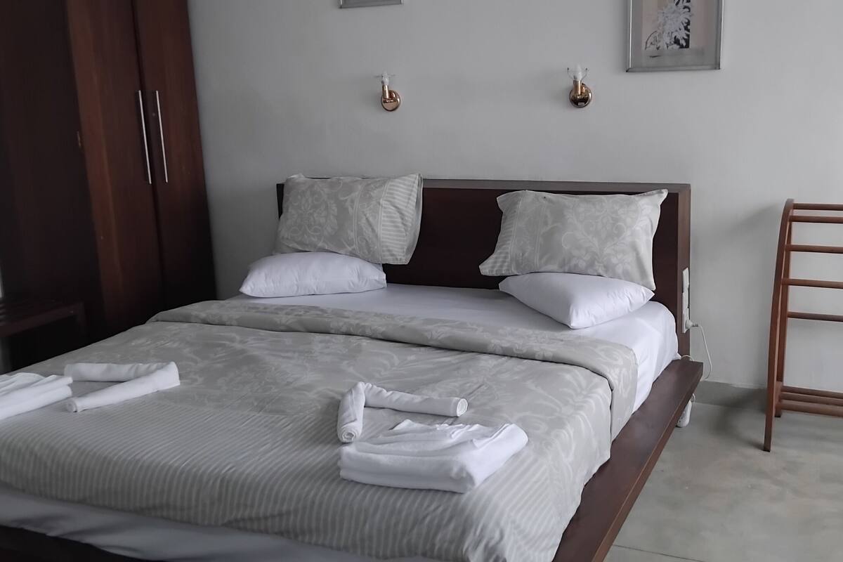 Una cama bien hecha con cabecera de madera, una mesita de noche y un perchero para toallas.