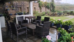An outdoor patio area with wicker furniture, a stone wall, and potted plants. - The Essence (Nuwara Eliya)