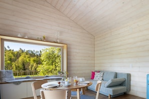 Interior acogedor de una cabaña con una mesa de comedor, zona de estar y un gran ventanal con vistas a un bosque.