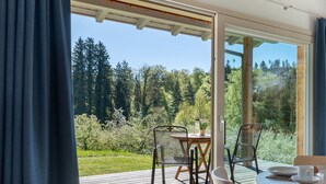 A room with a wooden deck, a table with chairs, and a view of a forest. - Time Out in Argental – Holiday Home Hagg near Lake Constance (Neukirch)