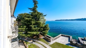 A balcony with a view of a clear blue lake, a large tree, and a stone pathway leading to a dock. - Apartment 'La Gioconda' with Lake View, Wi-Fi and Air Conditioning (Salò)