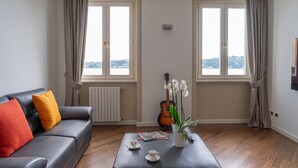 A living room with a sofa, a coffee table, a guitar, and a view through large windows. - Apartment 'La Gioconda' with Lake View, Wi-Fi and Air Conditioning (Salò)