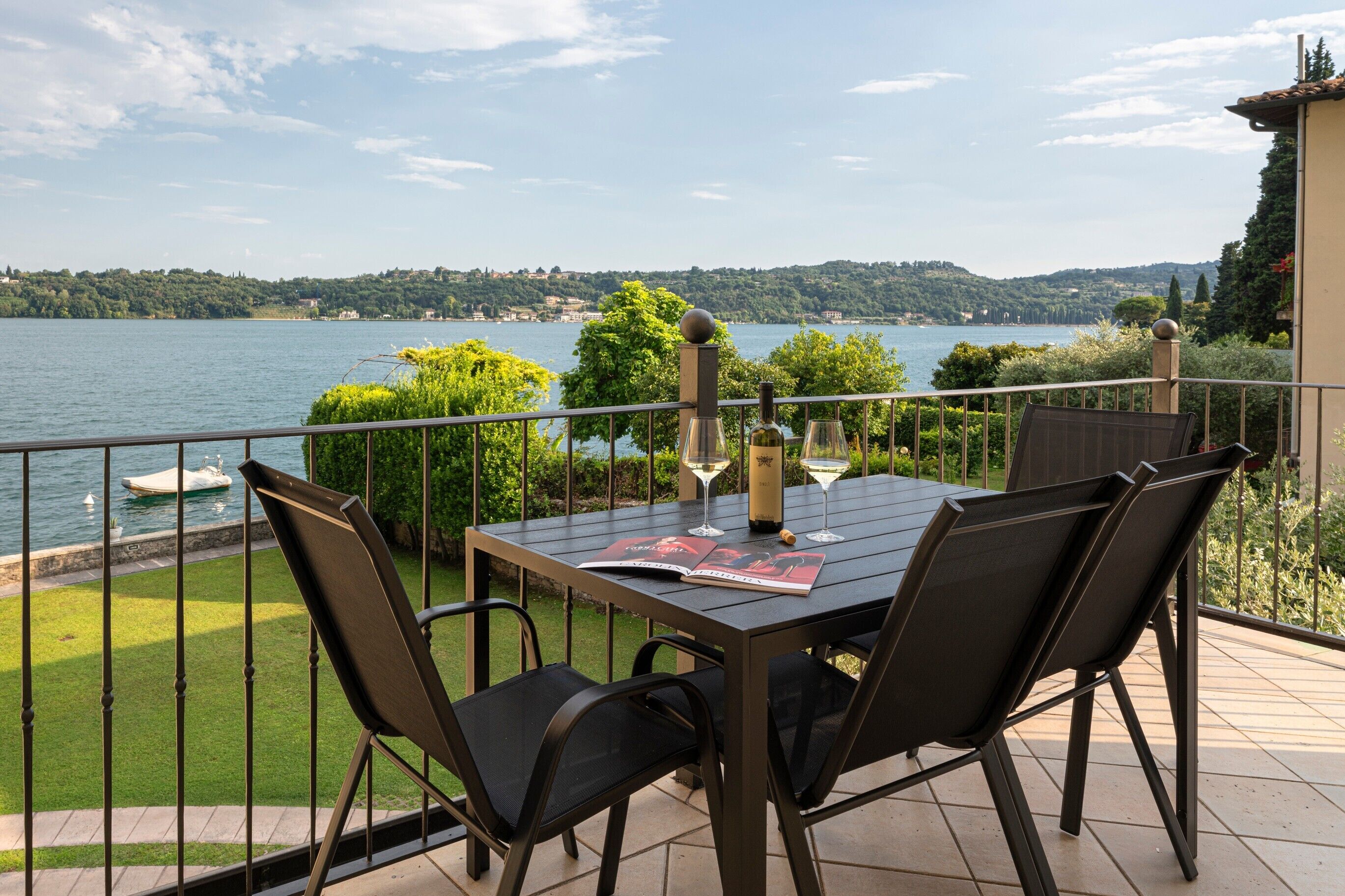 Area pranzo all'aperto con tavolo, sedie e vista sul lago.