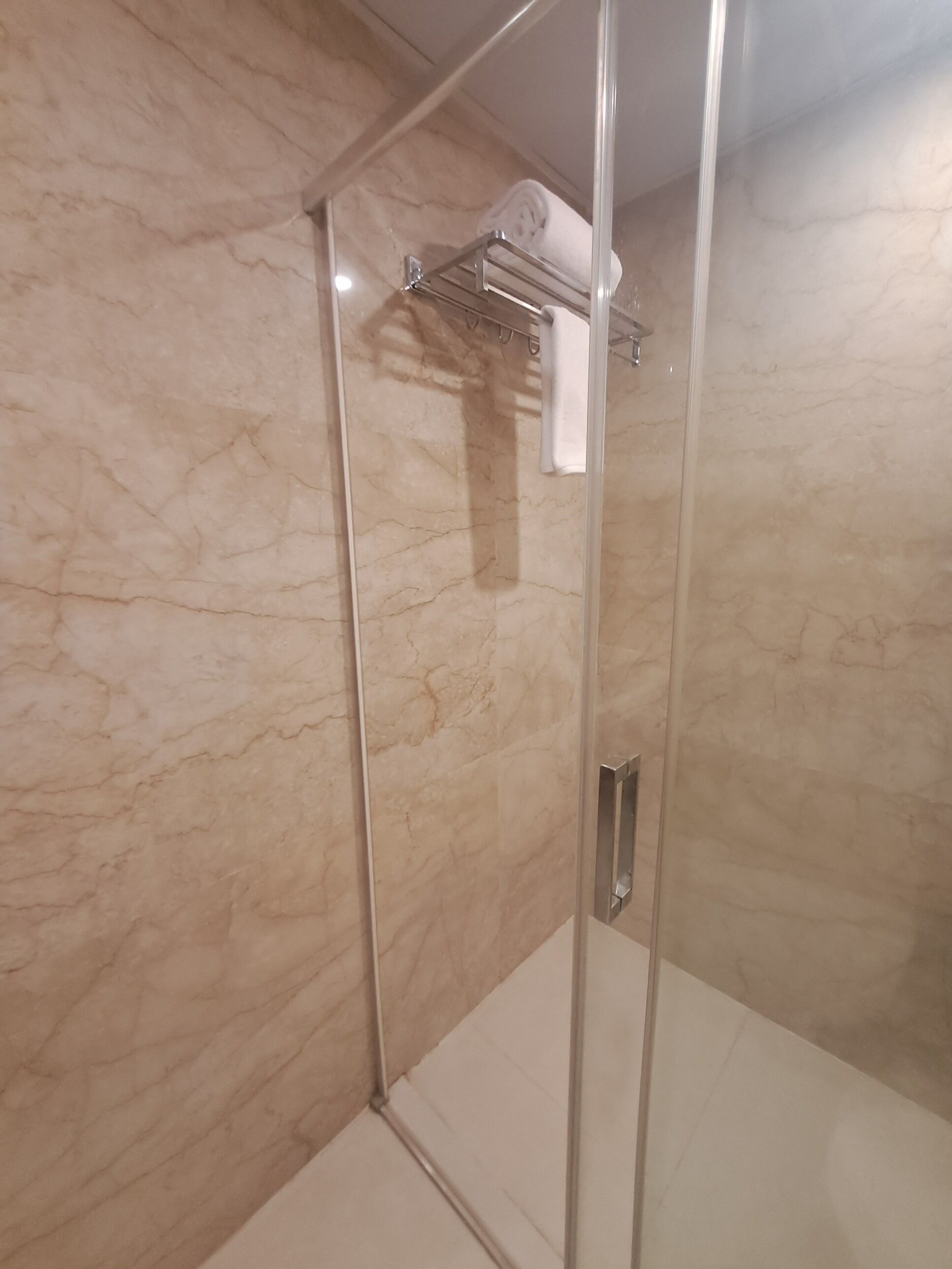 A glass-enclosed shower with a marble wall, a towel rack, and a visible shower control panel.