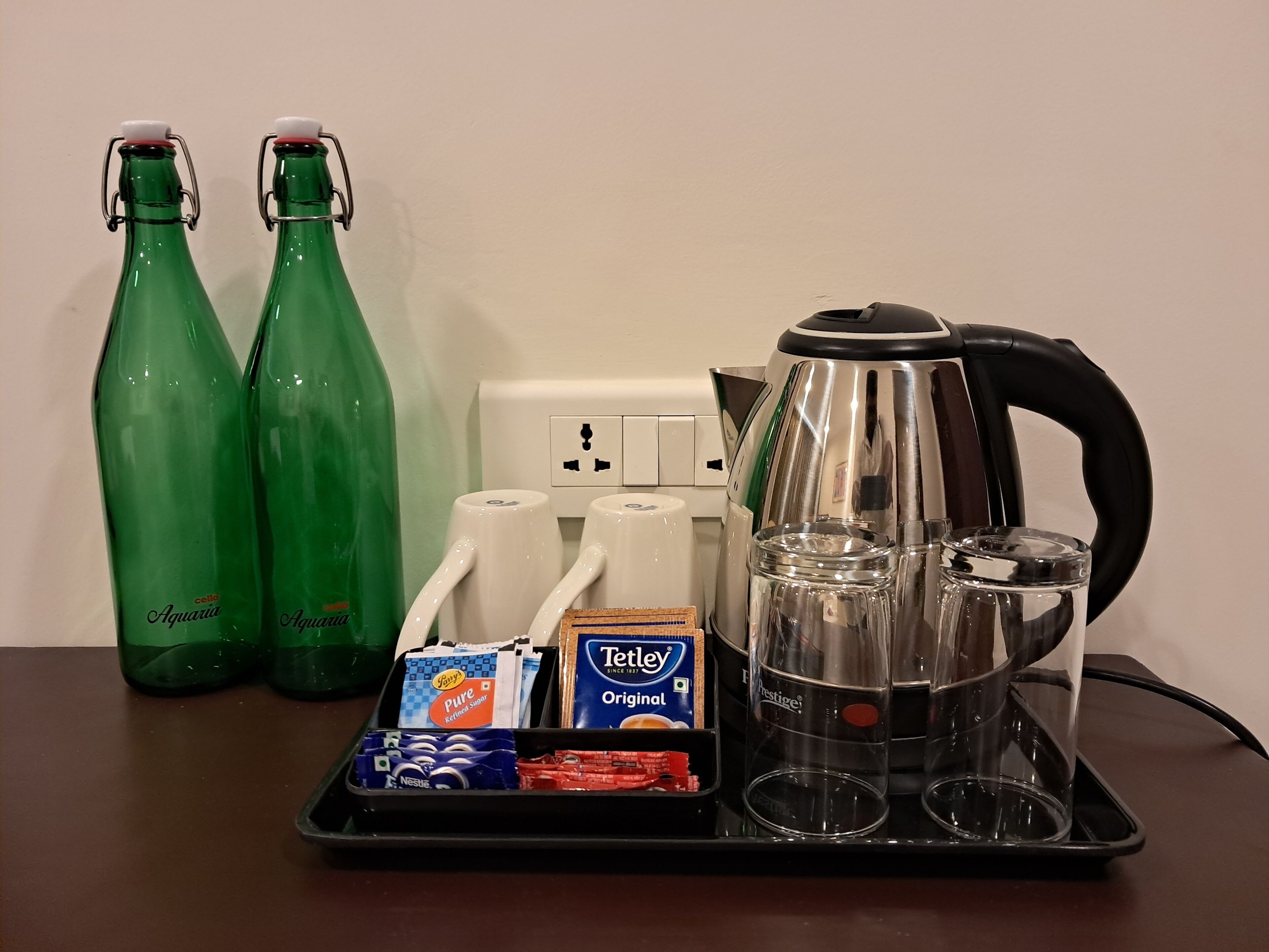 Un plateau avec deux bouteilles vertes, une bouilloire, des verres et une boîte de thé Tettey Original.
