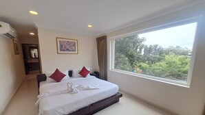 Habitación de hotel con una cama grande, una mesita de noche, un escritorio y una ventana con vistas al verdor.