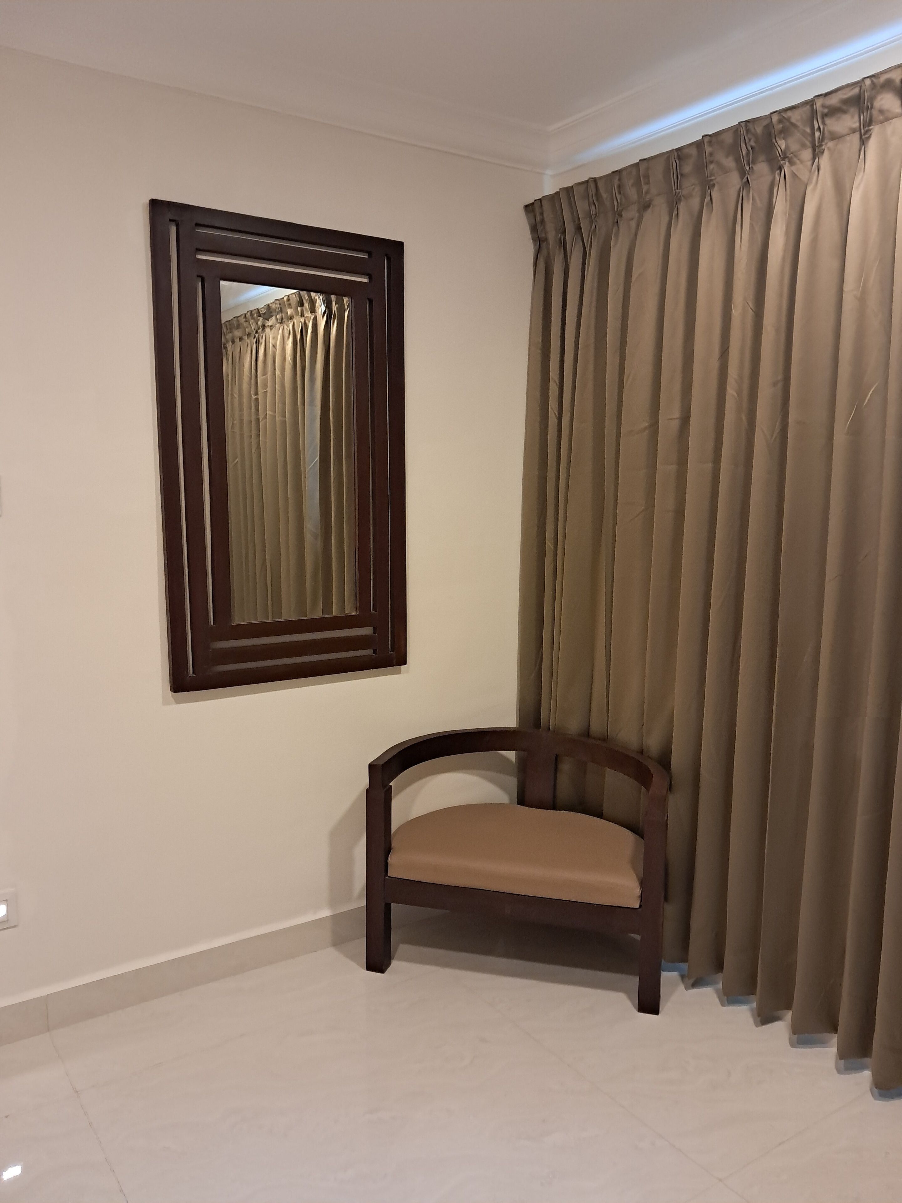 Una habitación con una silla de madera, un espejo grande y cortinas color beige.