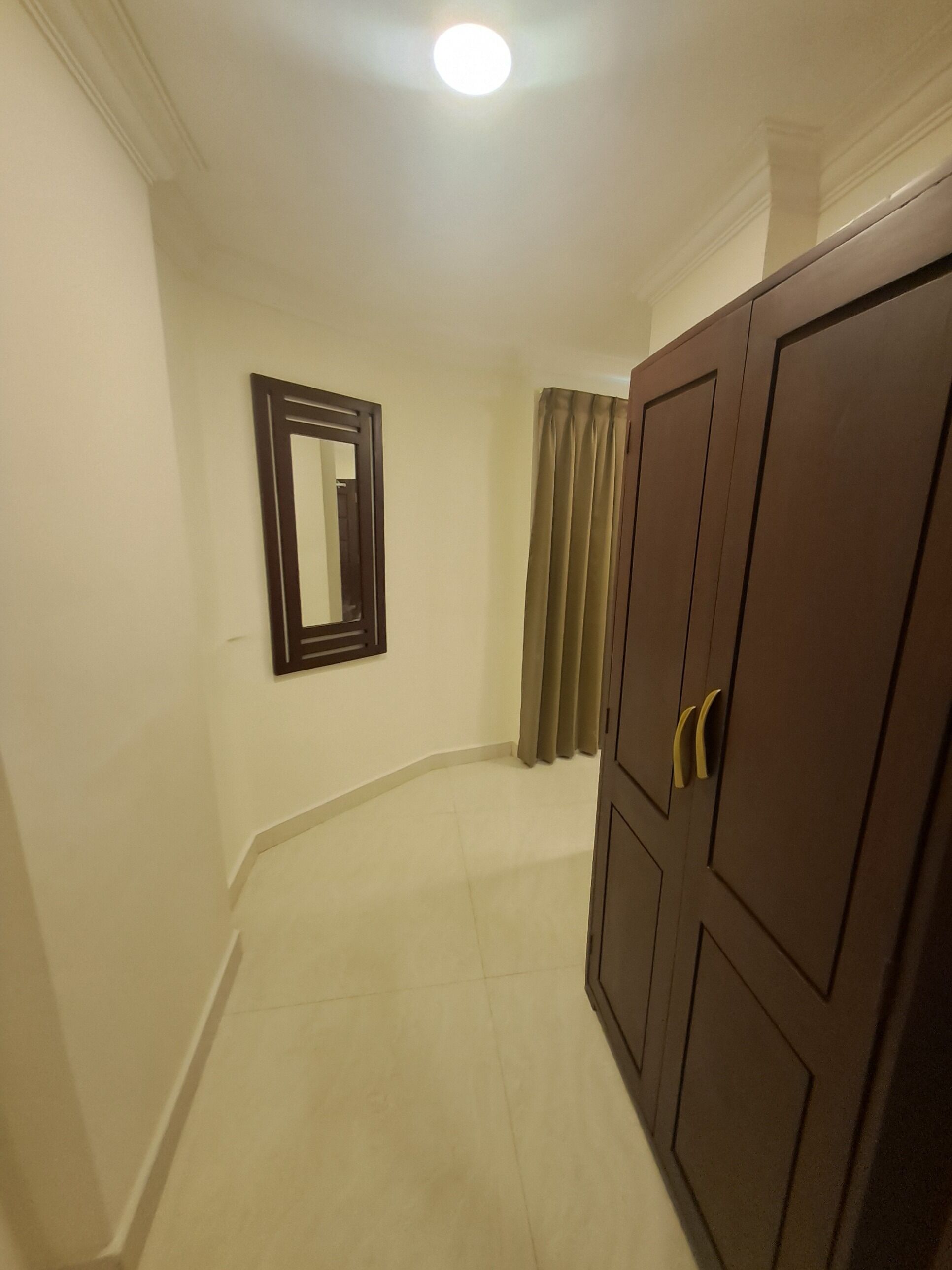 A hallway with a wooden wardrobe, a mirror on the wall, and a curtain.