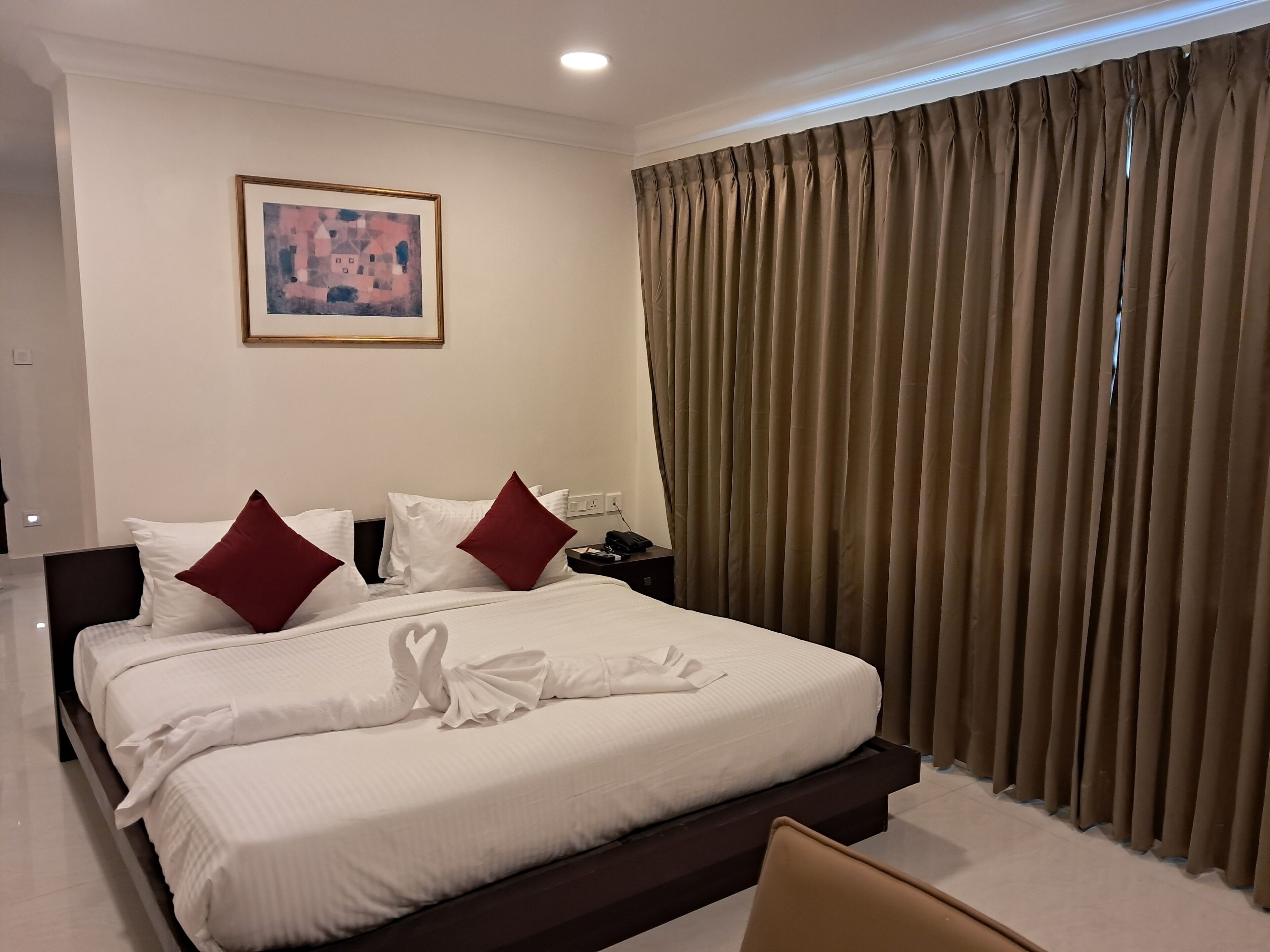 Una habitación de hotel con una cama bien hecha, un cuadro en la pared y un ventanal con cortinas.