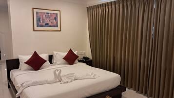 Una habitación de hotel con una cama bien hecha, un cuadro en la pared y un ventanal con cortinas.