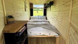Une petite pièce agréable et chaleureuse, avec un lit, un bureau en bois et une fenêtre donnant sur un espace verdoyant.