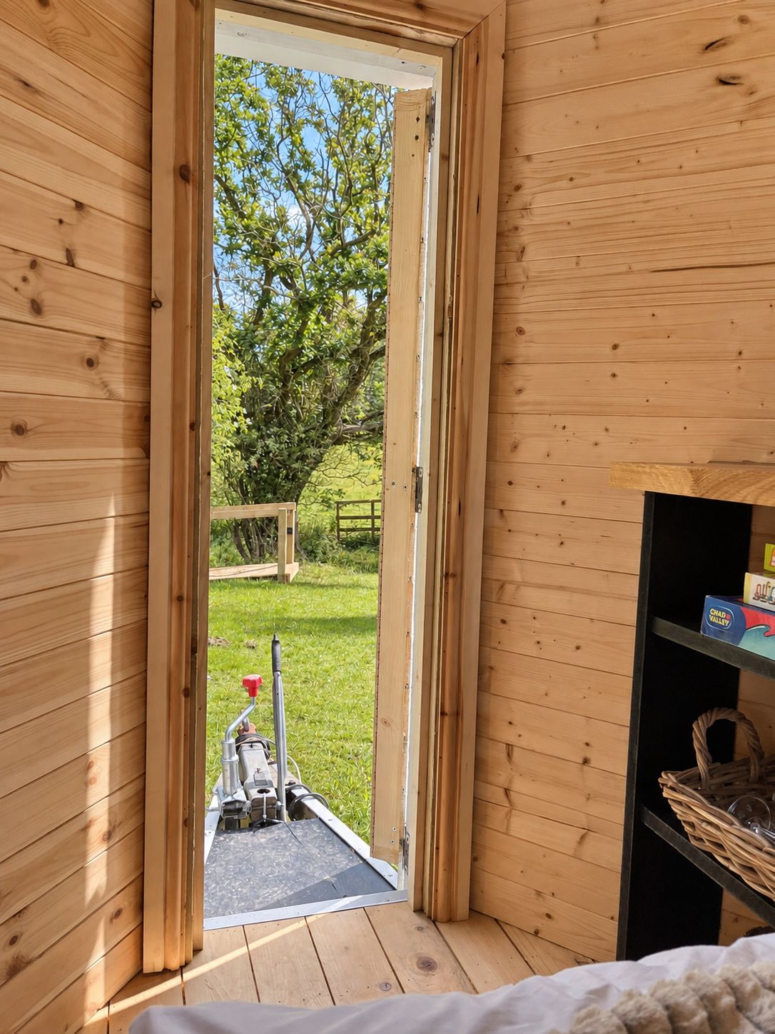 Une cabane en bois avec une porte donnant sur un espace extérieur comprenant une pelouse et un arbre.