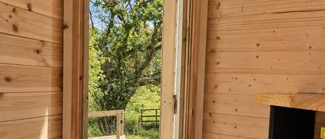 Une cabane en bois avec une porte donnant sur un espace extérieur comprenant une pelouse et un arbre.
