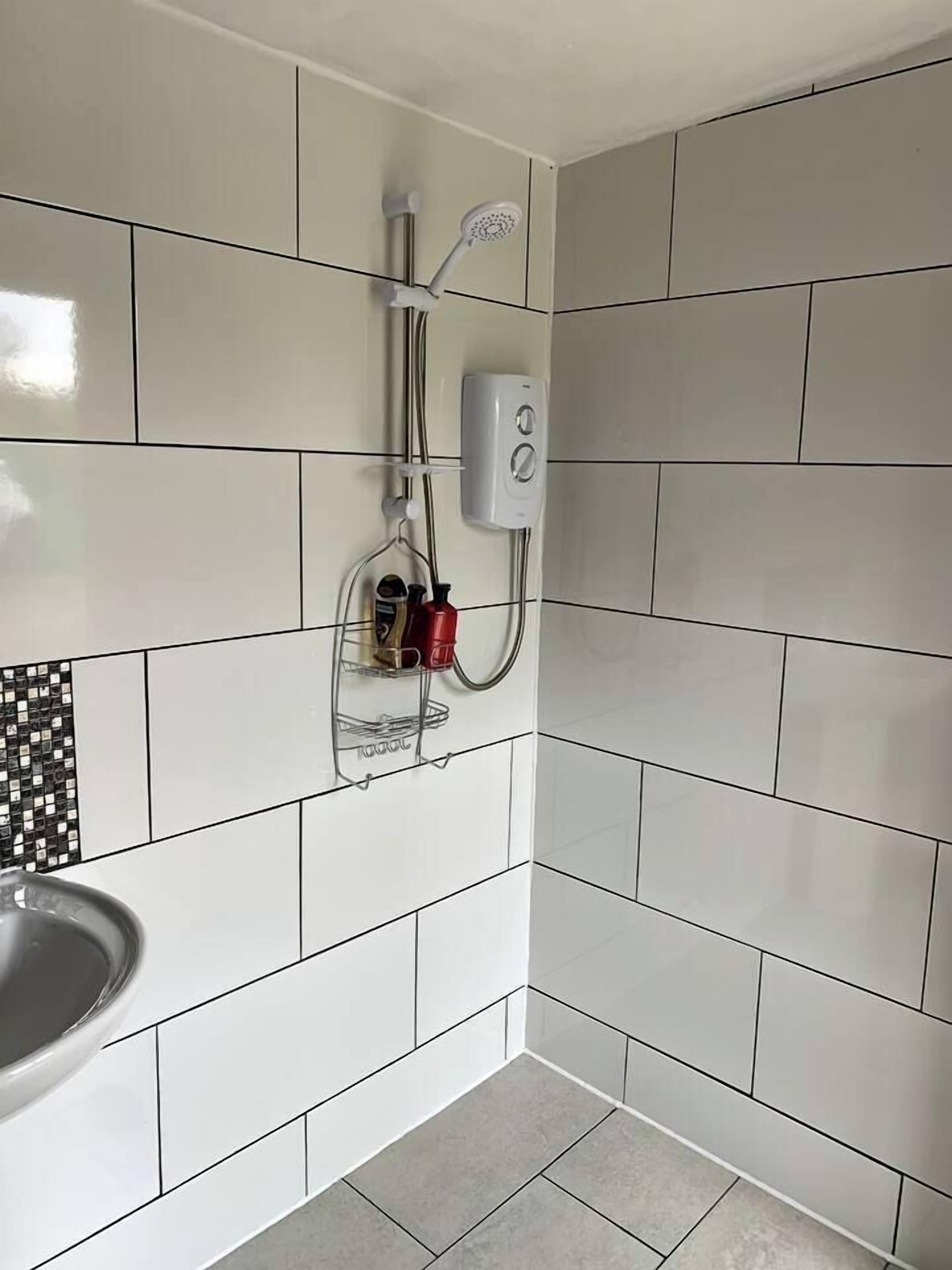 Une salle de bain avec des murs recouverts de carreaux blancs, une douche et un lavabo.