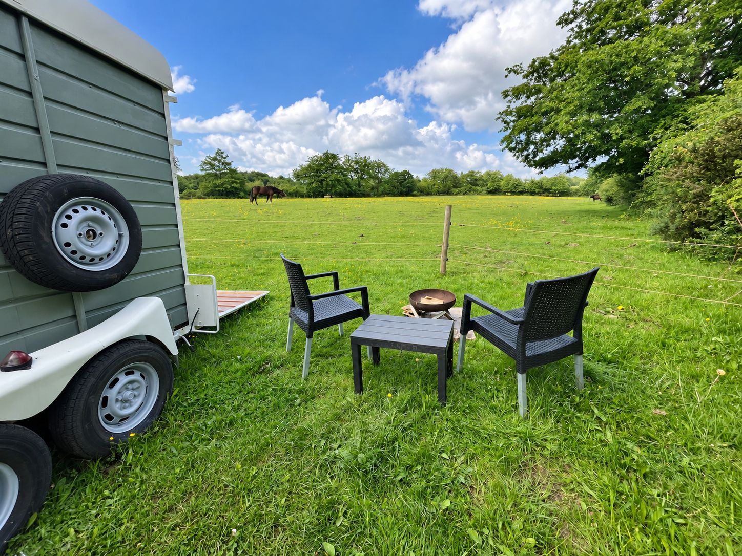 Un campo erboso con un camper, due sedie e un tavolo.