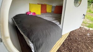 A cozy, circular room with a bed, colorful pillows, and a small window. - The Pig Sty - Farm Stay (Shepshed)